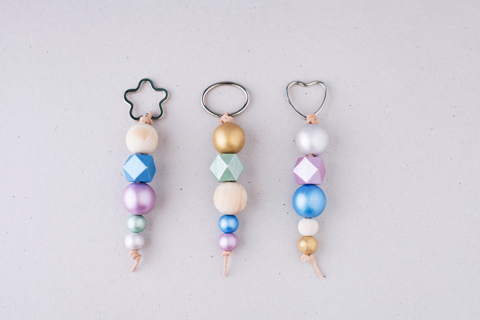 Keychains made of painted wooden beads with heart, star and oval shaped rings on a light background.